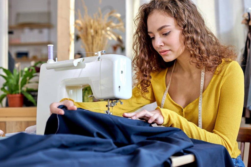 young tailor working on sewing machine, hand making clothes in home interior